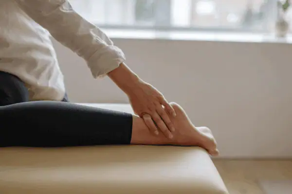 Person gently examining their foot and ankle on a treatment table, possibly experiencing pain from a stress fracture