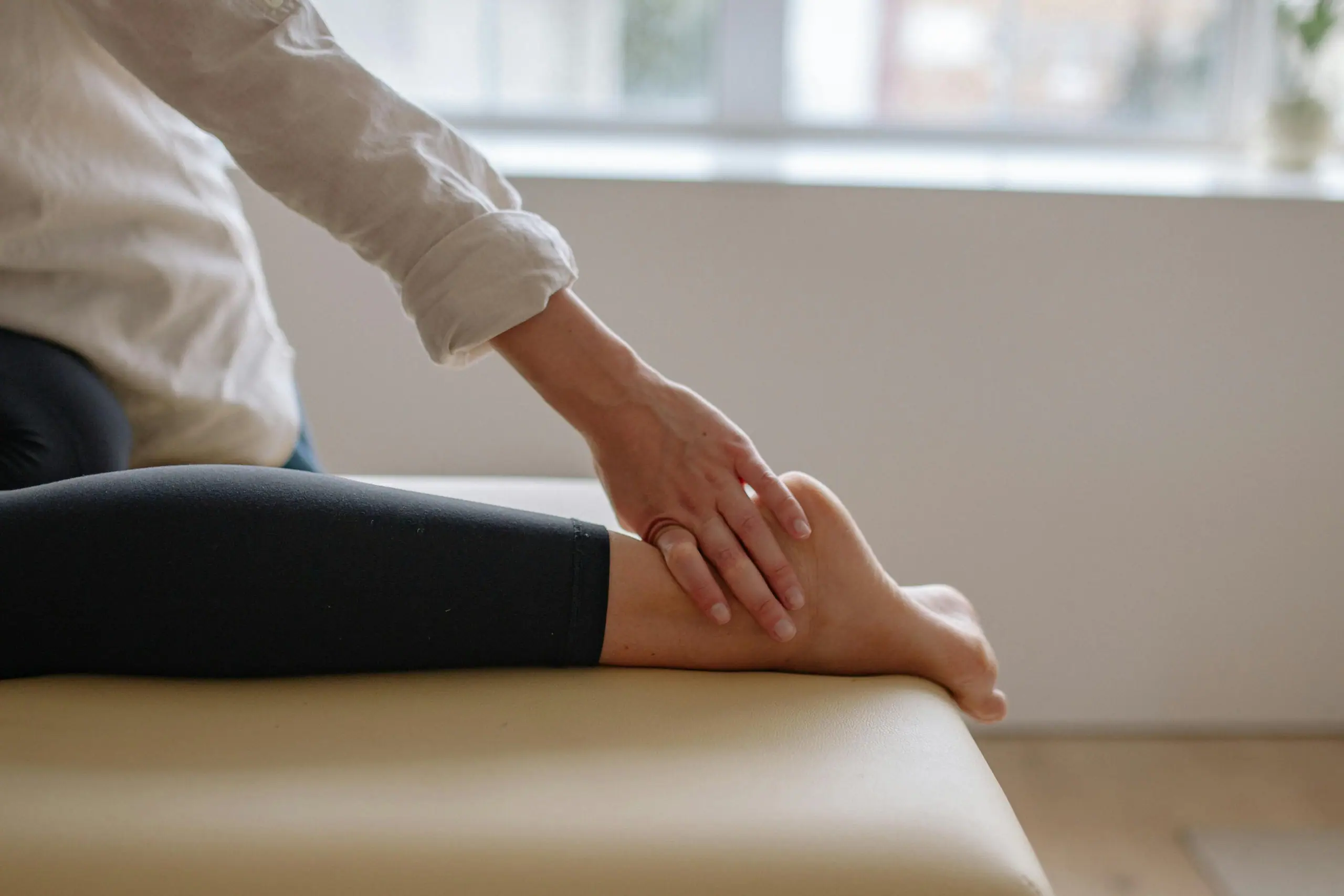 Person gently examining their foot and ankle on a treatment table, possibly experiencing pain from a stress fracture